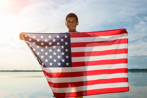 アフリカ系アメリカ人の男性はカメラを見て誇らしげにアメリカ国旗を持っています - 写真・画像