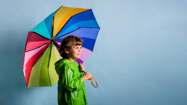 egy sokszínű esernyővel rendelkező kisfiú portréja kék alapon áll, szöveges hellyel. - Fotó, kép