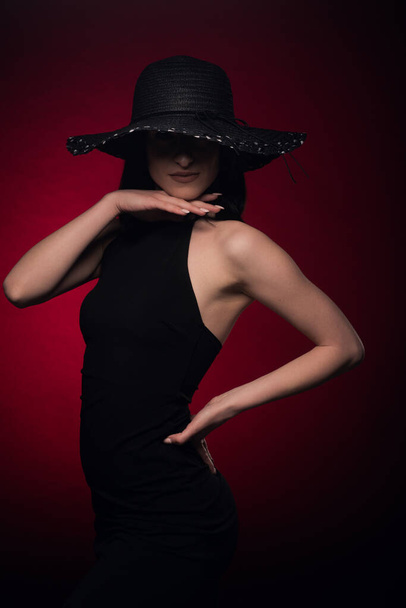 Chica seductora en vestido negro está posando en el set con su mano en la barbilla y la otra en la cadera - Foto, Imagen