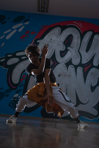 Mladý černoch tančí hip hop styl v městském prostředí. má na sobě oranžový oblek a je na graffiti pozadí. - Fotografie, Obrázek