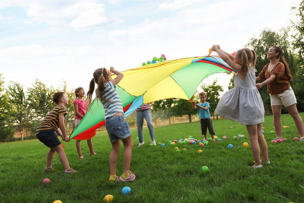 Group of children and teacher playing with rainbow playground parachute on green grass. Summer camp activity - Fotó, kép