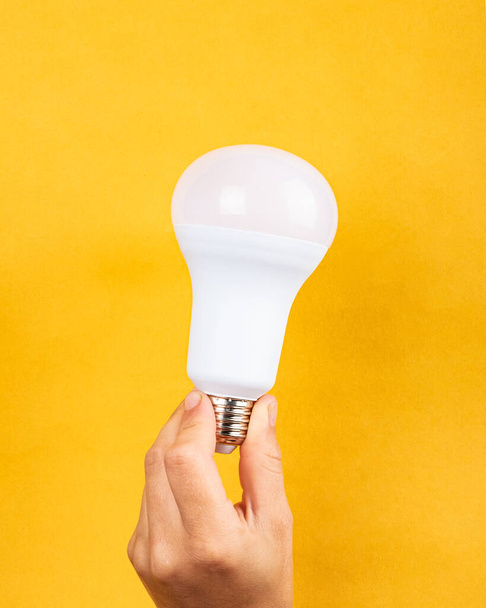 light bulb in hand on yellow background, electricity price increase concept - Foto, Imagen