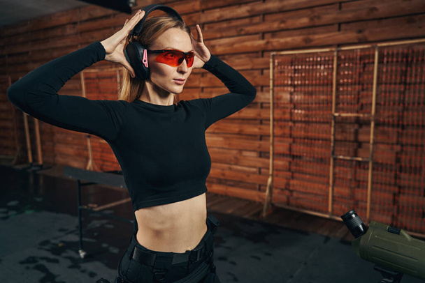 Ηρεμία γυναίκα shooter σε προστατευτικά γυαλιά και ακουστικά που στέκονται σε εσωτερικούς χώρους - Φωτογραφία, εικόνα