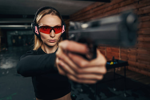 Fokussierter schöner Schütze mit Ohrenschützern, der eine Handfeuerwaffe schießt - Foto, Bild