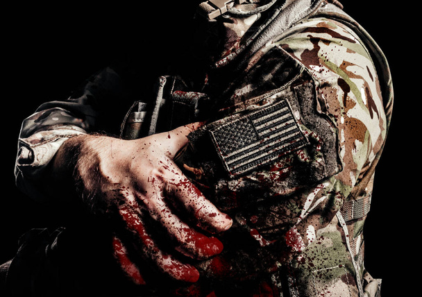 Foto sombreada e ferida soldado americano em uniforme com EUA patch no braço e respingo de sangue sobre ele. - Foto, Imagem