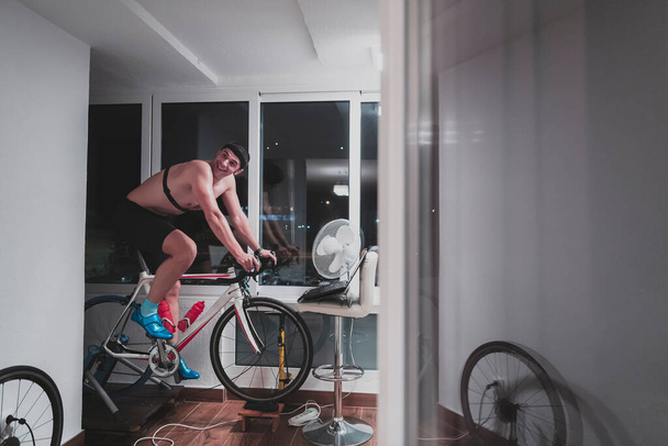 Motosiklet eğitmeni gece evde egzersiz yapıyor ve çevrimiçi bisiklet yarışı oynuyor. - Fotoğraf, Görsel