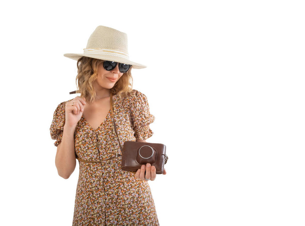 Kobieta w okularach przeciwsłonecznych, brązowa sukienka w kapeluszu z kamerą retro na białym tle. - Zdjęcie, obraz