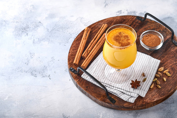 Turmeric golden milk latte with cinnamon sticks and honey. Healthy ayurvedic drink. Trendy Asian natural detox beverage with spices for vegans. Copy space. - Photo, Image