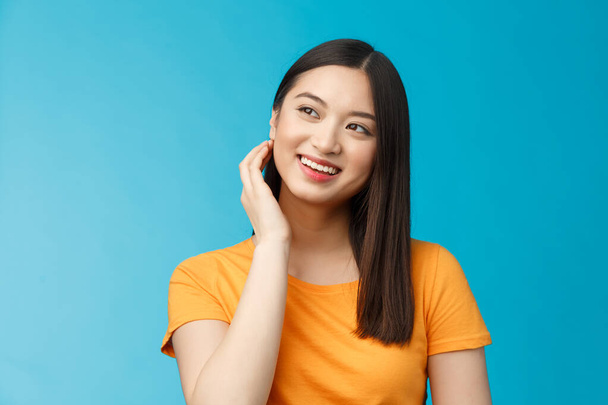Tender lovely coquettish modern asian woman touch hair lovely look aside, smiling joyfully, feel satisfied after good haircut, deal with nasty pimples, get rid acne delighted, stand blue background - Photo, Image