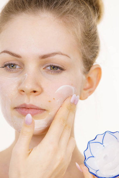Young woman applying cream cosmetic, mask moisturizing to her face. Beauty treatment. Skincare. - Foto, Bild