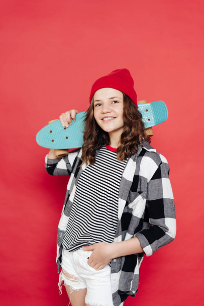 Belle adolescente posant avec penny board sur fond rouge - Photo, image