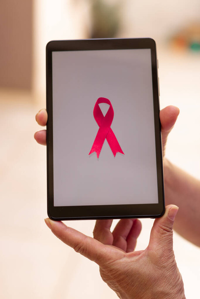Dojrzała kobieta trzyma tabletkę z różową wstążką. Miesiąc świadomości raka piersi z wizerunkiem technologii.  - Zdjęcie, obraz