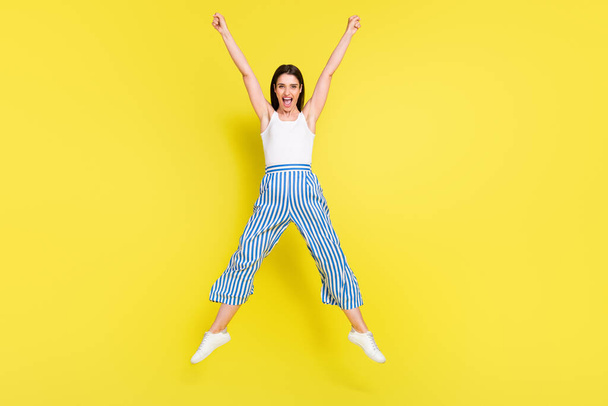Full body photo of funky brunette young lady jump yell wear top pants sneakers isolated on yellow color background - Foto, imagen