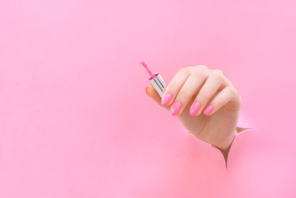 brush with nail polish in the hand of a young woman on a pink background from the hole. copy space - Foto, Imagem