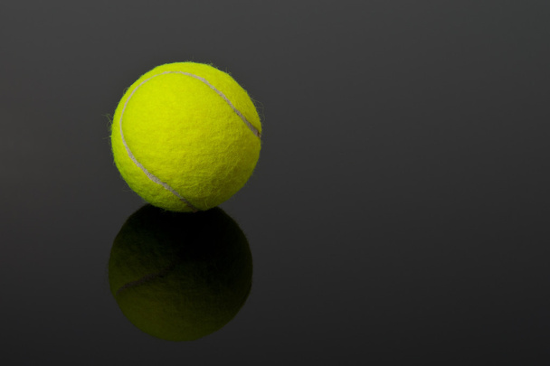 Желтый теннисный мяч на черном фоне с тенью
 - Фото, изображение