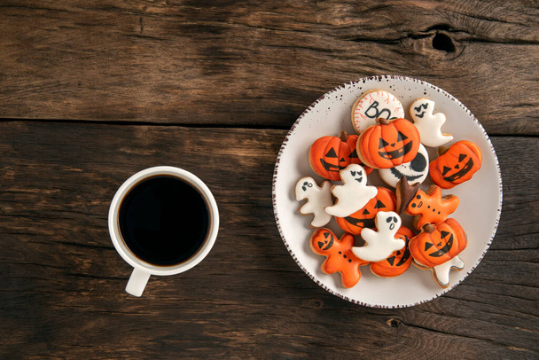 Cup of delicious aromatic coffee and funny gingerbread on Halloween stand on a brown wooden surface. pumpkin and ghost . - Photo, Image