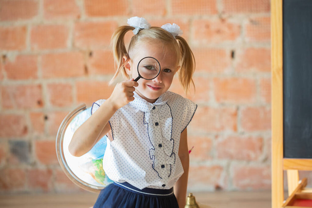 Adorable caucasian private school kindergarten girl with magnifier if front of her eye, back to school concept - Foto, afbeelding