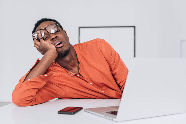 Müder afroamerikanischer Mann schläft angelehnt an Laptop - Foto, Bild
