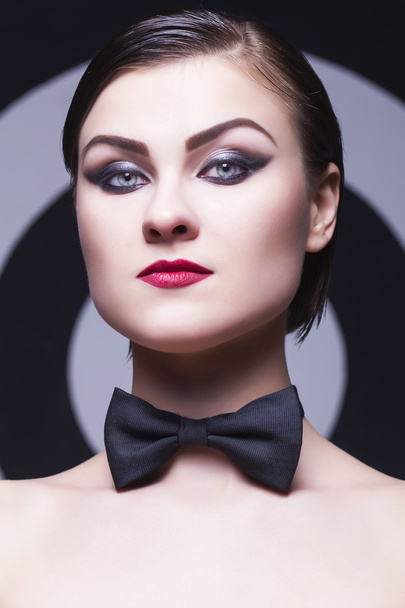 Pretty woman with evening make up and red lips in a bow-tie in a center of a dartboard background - Foto, Imagen