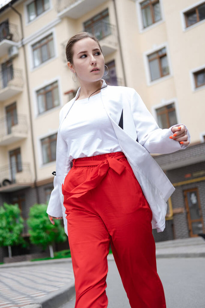 επιχειρηματίας με κόκκινα παντελόνια, λευκή μπλούζα και σακάκι περπατώντας στο δρόμο. - Φωτογραφία, εικόνα