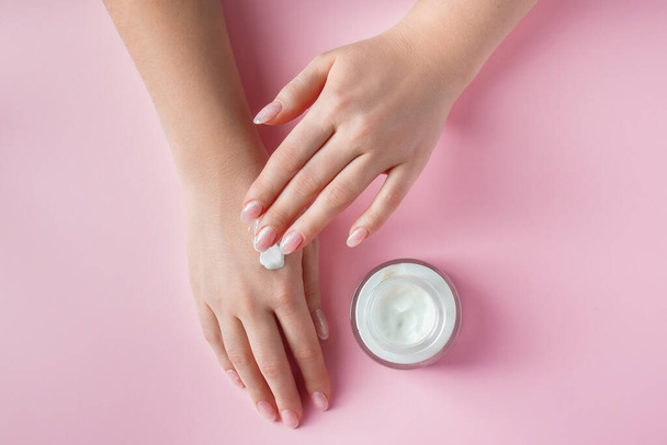 Weibliche Hände mit einer Flasche Sahne auf rosa Hintergrund. Wellness- und Körperpflegekonzept. Image für die Werbung. - Foto, Bild