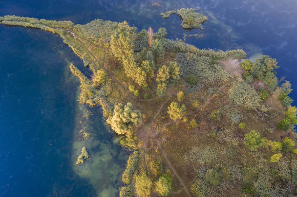 Egy kis sziget a tó közepén, sárga őszi levelek a fákon. Drónra néző. - Fotó, kép