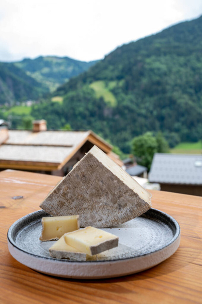 Käsekollektion, französischer Käse tomme de savoie und französisches Bergdorf in Haute-Savoie im Sommer im Hintergrund - Foto, Bild
