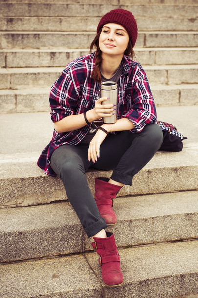 Brunette woman in hipster outfit sitting on steps on the street. Toned image - Foto, Imagen
