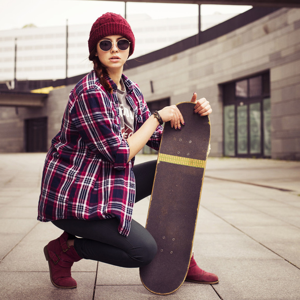 brunetka kobieta w stroju hipster siedzi na zworki na ulicy. stonowanych obrazu - Zdjęcie, obraz