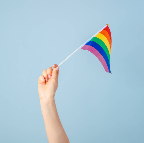 Closeup of a hand waving a small rainbow flag against a light blue background - Foto, Imagem