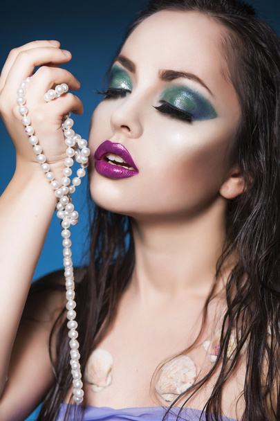 Belle femme sirène brune avec maquillage créatif et perles perlées dans sa main. Yeux fermés
 - Photo, image
