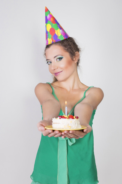 ケーキのろうそくの火を吹いて誕生日キャップのブルネットの女性 - 写真・画像