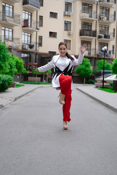 Kırmızı pantolonlu, beyaz bluzlu, ceketli, kendine güvenen esmer kadın sokakta yürüyor.. - Fotoğraf, Görsel