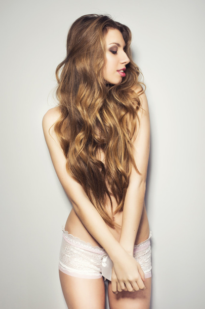 Hermosa mujer rubia con el pelo largo usando solo bragas cerca de la pared en pose sexy sonriendo
 - Foto, Imagen