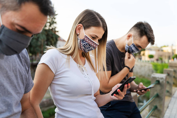 Side view on caucasian man and woman using mobile phone - Modern communication online texting social network messaging - Men and woman with mask hold mobile phones - social distance new normal concept - Photo, Image
