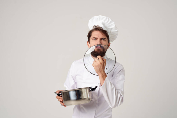 Üniformalı bir adam elinde tavayla restoran endüstrisini pişiriyor. - Fotoğraf, Görsel