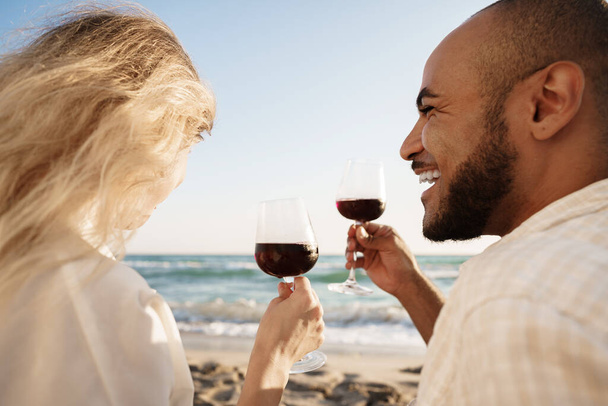Portrait of a young couple sitting on the beach and drinking wine - 写真・画像