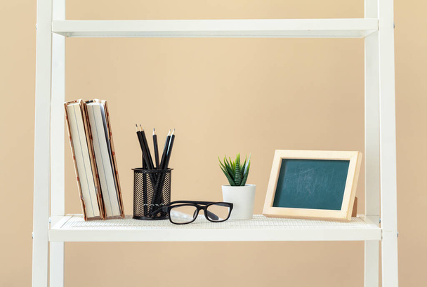 White bookshelf with books and stationery against beige wall - Foto, afbeelding