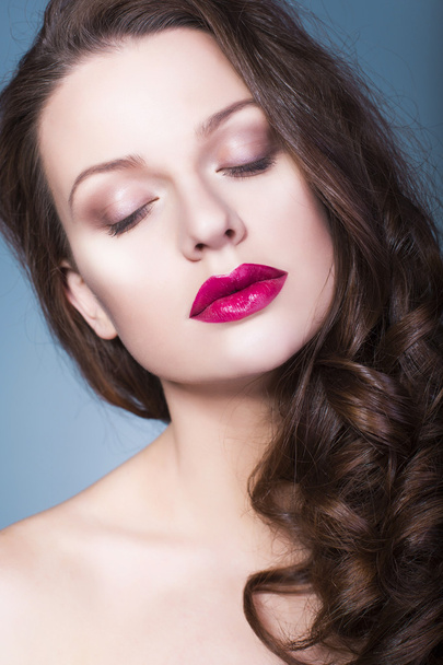 Belle femme brune avec maquillage créatif ombres à paupières violettes lèvres rouges pleines, yeux bleus et cheveux bouclés avec sa main sur son visage
 - Photo, image