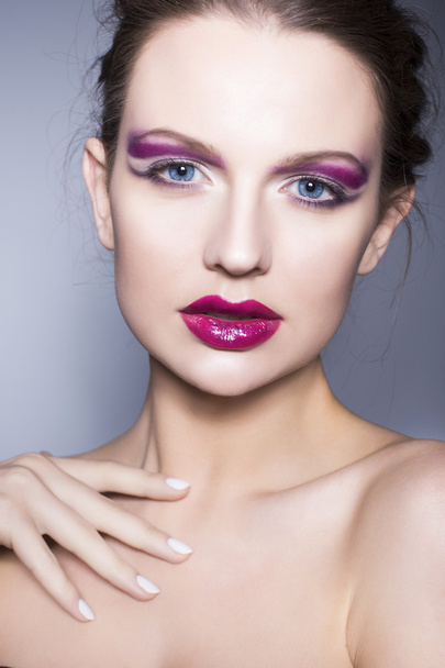 Красива брюнетка з креативним макіяжем фіолетові тіні для очей повні червоні губи, блакитні очі і кучеряве волосся з її рукою на обличчі
 - Фото, зображення