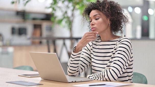 Afrikaanse vrouw denken en werken op laptop in kantoor - Foto, afbeelding