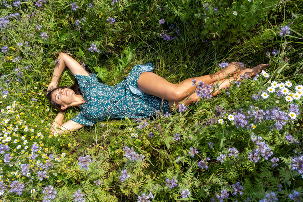 beautiful slender brunette lies in a field among wildflowers - Foto, afbeelding