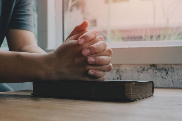 Woman with Bible praying, hands clasped together on her Bible on wooden table. - Photo, image
