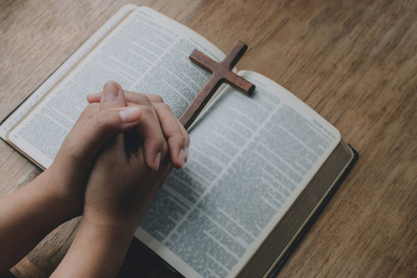 Donna con croce di legno in mano che prega per la benedizione di Dio sul vecchio libro della Bibbia. Spirtualità e religione, Concetti religiosi - Foto, immagini
