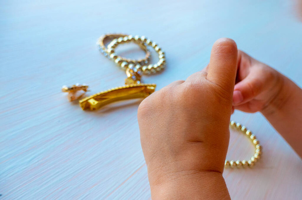 ruce dítěte hrát se zlatými šperky a bižuterie, na bílém pozadí. koncept ženského štěstí Vysoce kvalitní fotografie - Fotografie, Obrázek