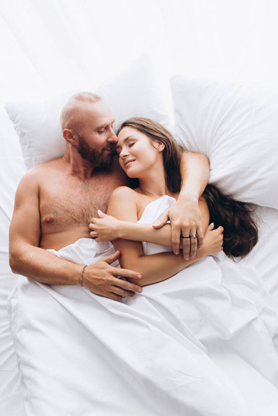 Loving couple in bed on white sheets. Stay at home. - 写真・画像