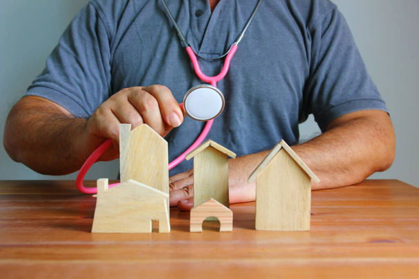 Asian man using stethoscope checking wooden model home on wood floor - Foto, immagini