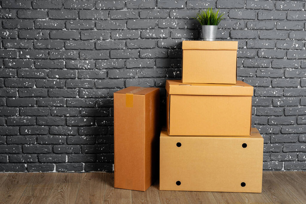 Stack of cardboard boxes in the empty room against black brick wall - Φωτογραφία, εικόνα
