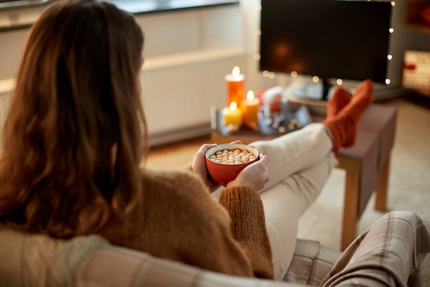 woman watches tv and drinks cocoa on halloween - Foto, afbeelding