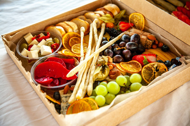 Lahodné vinné občerstvení v kartonové krabici na bufet na párty: sýry, klobásy, studené kousky, ovoce, bageta, Grissini - Fotografie, Obrázek